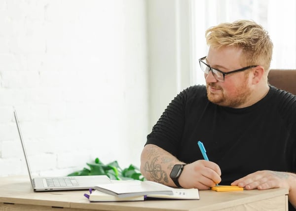 Worker takes notes while looking at laptop